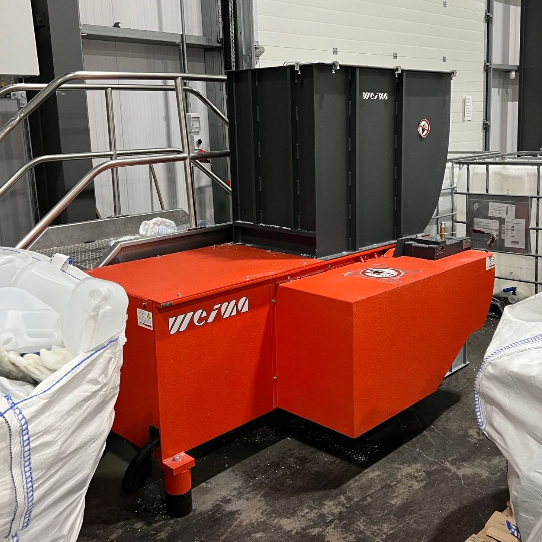An orange shredder in a production hall between big bags filled with plastic production waste