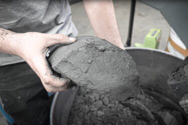 man holding piece of dried grinding sludge above a full barrel