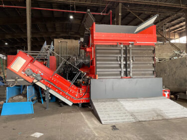 An orange shredder shreds municipal waste in a recycling plant.