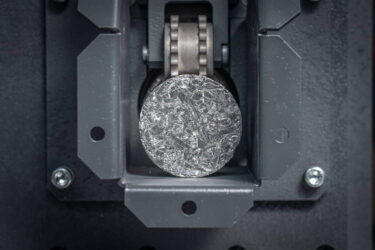 Ein rundes Metallbrikett im Austrag einer Brikettierpresse