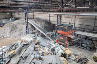 Ansicht von oben auf einen WEIMA Shredder mit Förderband. Material zur Zerkleinerung liegt im Bereich vor dem Shredder, nach dem Förderband kommt das zerkleinerte Material