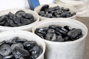 Ausrangierte schwarze PVC Pucks für das Recycling, in weißem Kunststoffbehälter gesammelt
