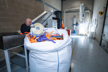 PVC Recyclinganlage bei Record Industry mit WEIMA Shredder, Wanner Granulator, Entstaubung, links befüllt ein Mitarbeiter ein Förderband mit Schallplatten Produktionsresten