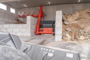 Gesamtansicht der Anlage im Brennholzwerk Trier mit WEIMA Zerkleinerer, roter Steiner-Förderschnecke und großem Restholzlager.